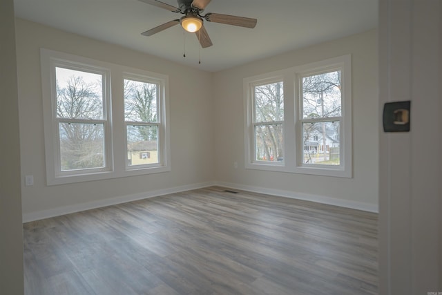 spare room with ceiling fan, visible vents, baseboards, and wood finished floors