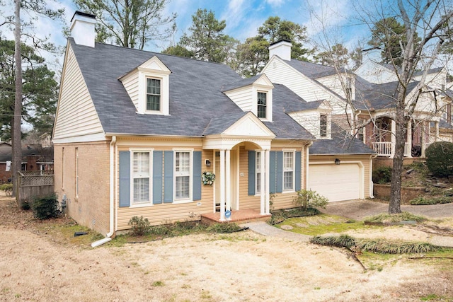 new england style home with an attached garage, a chimney, and brick siding