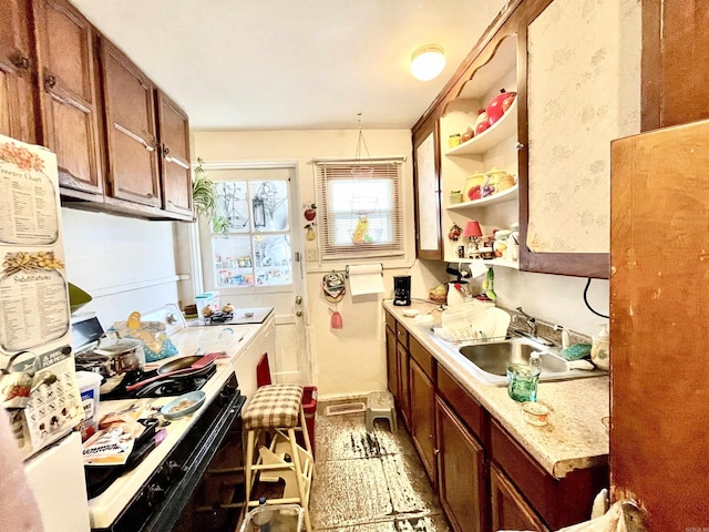 kitchen featuring light countertops, black range with electric cooktop, a sink, and brown cabinets