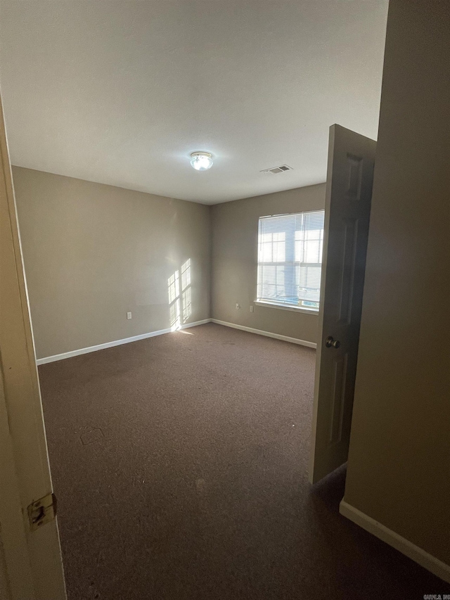 empty room with visible vents, dark carpet, and baseboards