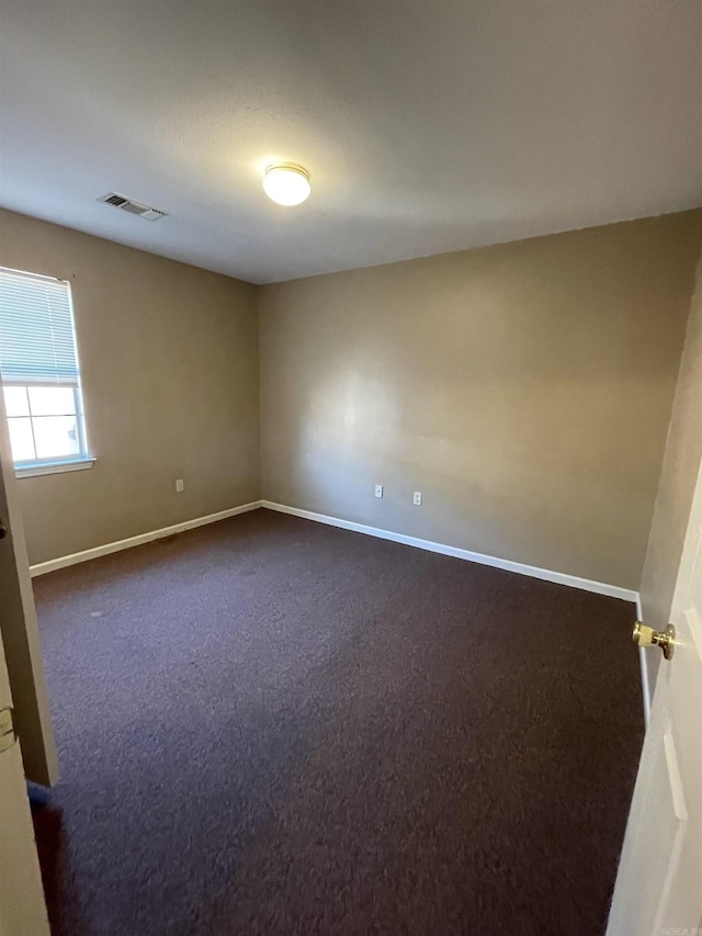 spare room with visible vents, dark carpet, and baseboards