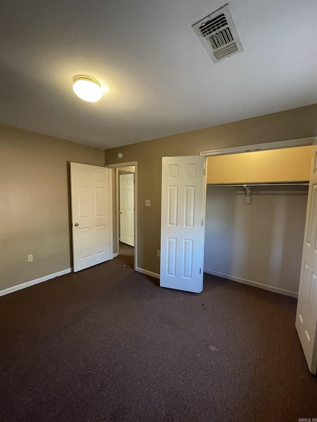 unfurnished bedroom with dark colored carpet, a closet, visible vents, and baseboards