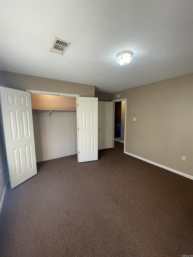 unfurnished bedroom with baseboards, visible vents, dark carpet, and a textured ceiling