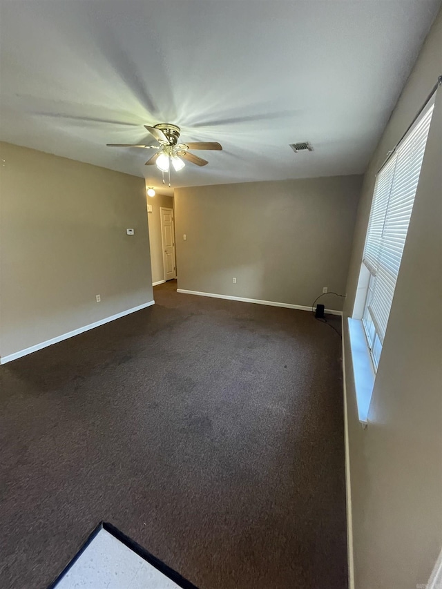 empty room featuring a ceiling fan, visible vents, dark carpet, and baseboards