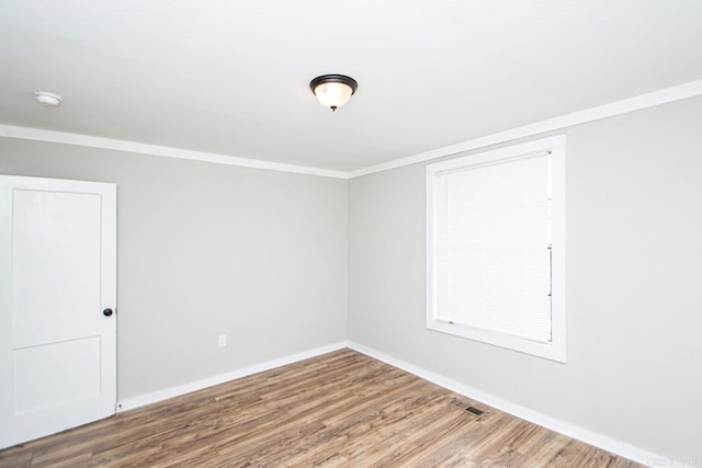 empty room with baseboards, visible vents, ornamental molding, and wood finished floors