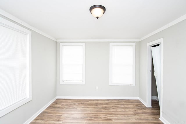 unfurnished room with crown molding, plenty of natural light, wood finished floors, and baseboards