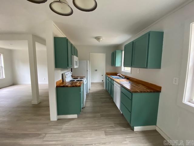 kitchen with white appliances, light wood finished floors, green cabinetry, wood counters, and a sink