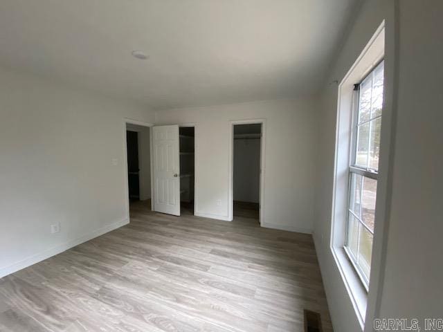 unfurnished bedroom featuring light wood-type flooring, visible vents, baseboards, and multiple closets