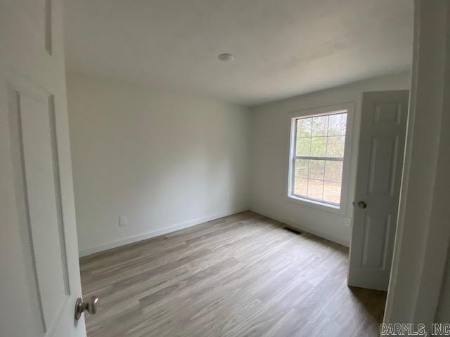 unfurnished room featuring wood finished floors, visible vents, and baseboards