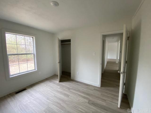 unfurnished bedroom with a closet, light wood-type flooring, visible vents, and baseboards