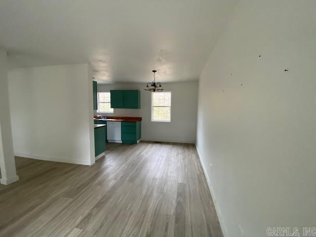 unfurnished living room featuring a chandelier, light wood-style flooring, and baseboards