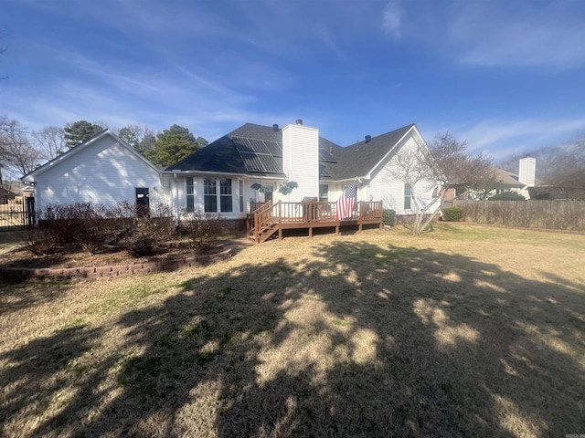 rear view of house featuring fence, a lawn, a chimney, and a wooden deck