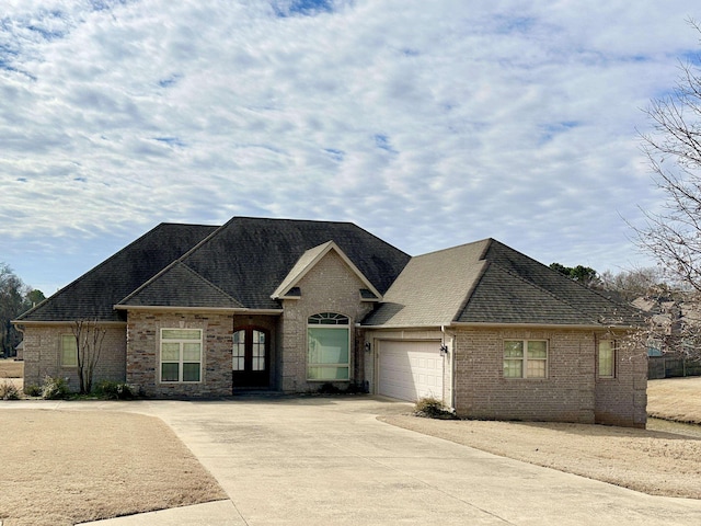 view of front of property featuring a garage, driveway, brick siding, and roof with shingles