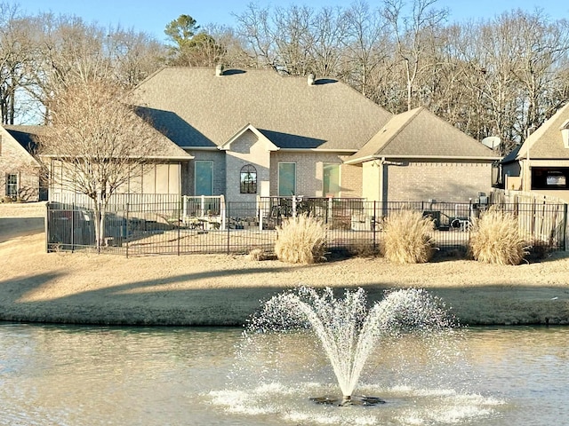 view of front of property featuring brick siding, fence, and a water view