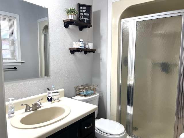 bathroom featuring a textured wall, a stall shower, vanity, and toilet