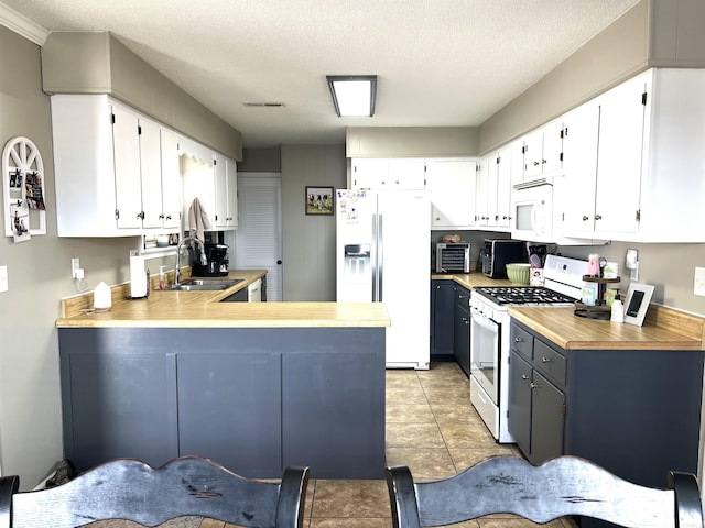 kitchen featuring light countertops, visible vents, a sink, white appliances, and a peninsula
