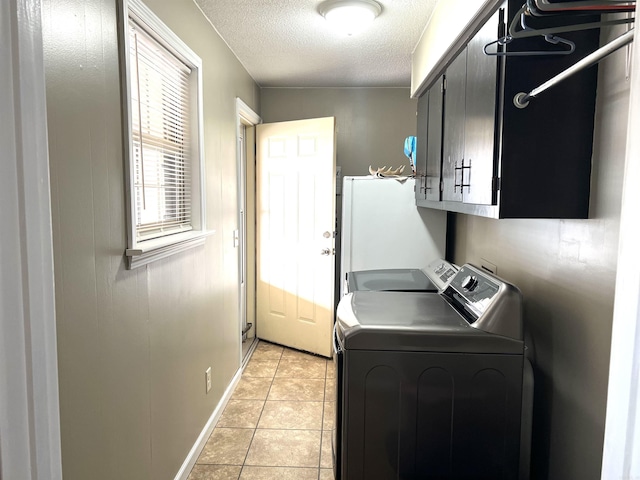 laundry room featuring a textured ceiling, light tile patterned floors, separate washer and dryer, baseboards, and cabinet space