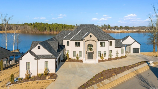 french country home featuring concrete driveway, a water view, and an outdoor structure