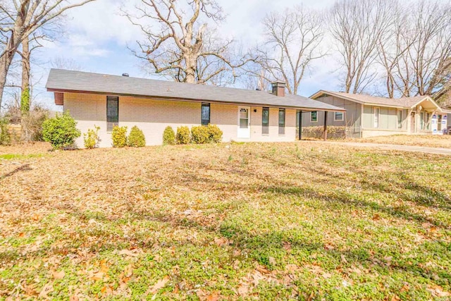 ranch-style home featuring a front yard, brick siding, and a chimney