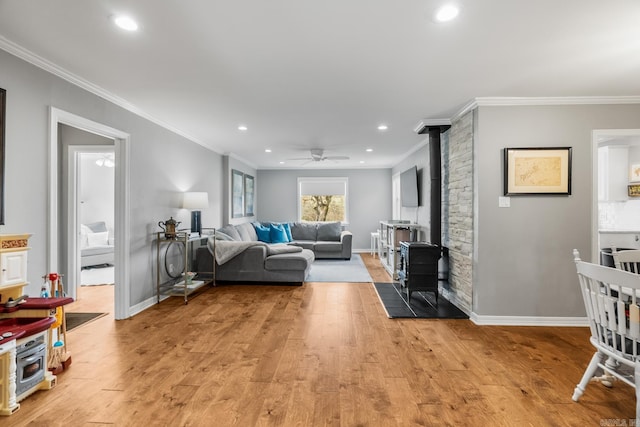 living room featuring a ceiling fan, light wood-style flooring, a wood stove, crown molding, and recessed lighting