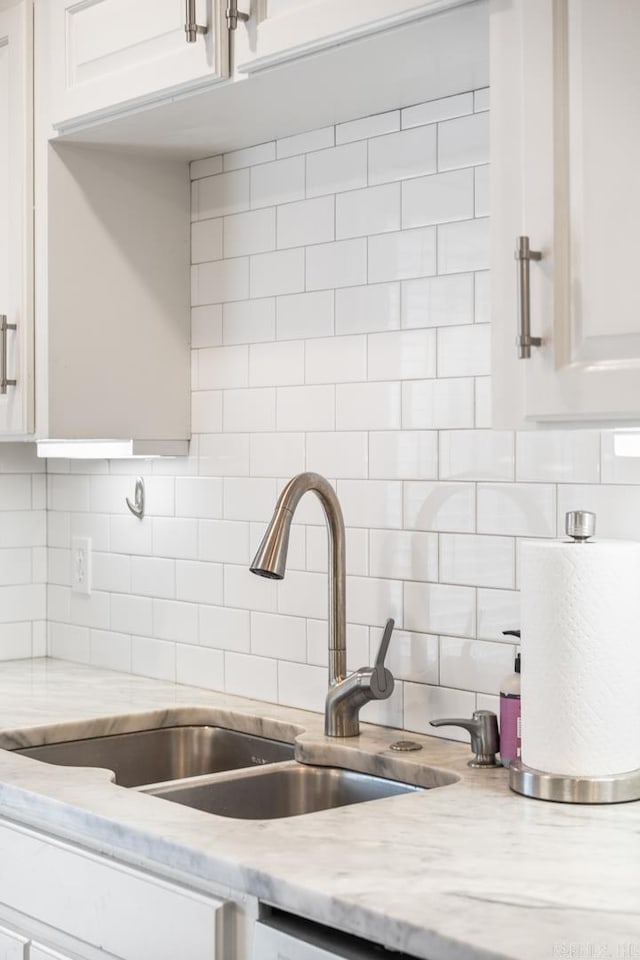 kitchen featuring tasteful backsplash, white cabinetry, a sink, and light stone countertops