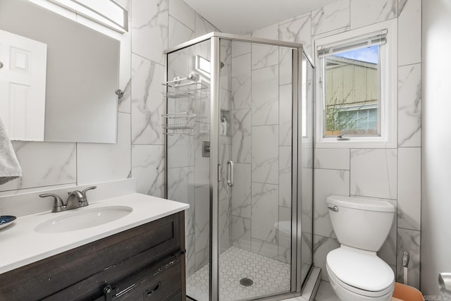 full bath with vanity, a marble finish shower, toilet, and tile walls