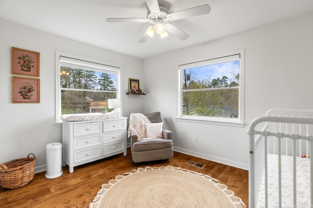 bedroom with a crib, baseboards, visible vents, and wood finished floors