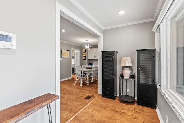 hall with light wood-style floors, visible vents, baseboards, and crown molding