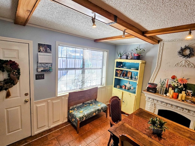 interior space with a textured ceiling, wainscoting, a fireplace, and beam ceiling