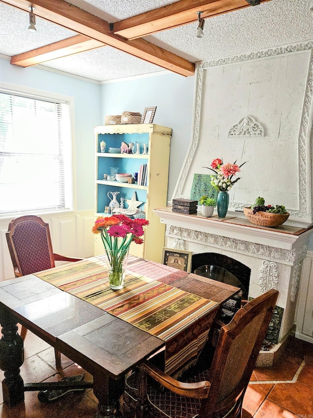 dining space featuring a textured ceiling, a decorative wall, a premium fireplace, wainscoting, and beamed ceiling