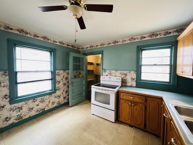 kitchen featuring a sink, electric stove, light countertops, wainscoting, and wallpapered walls