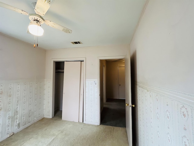 unfurnished bedroom featuring visible vents, a wainscoted wall, ceiling fan, carpet floors, and a closet