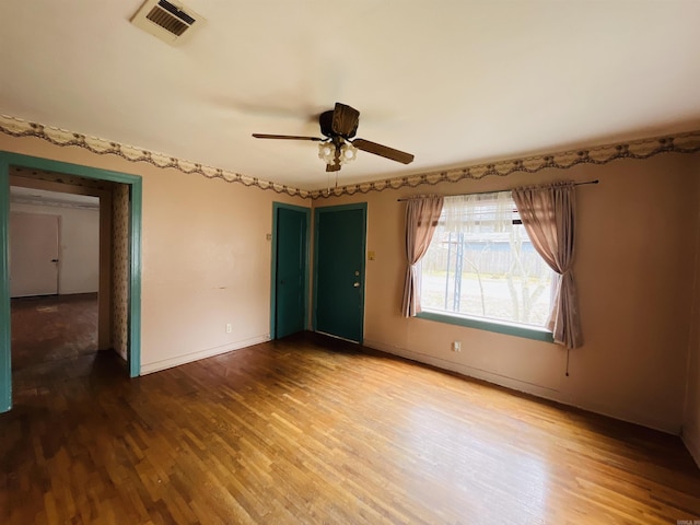 spare room with a ceiling fan, visible vents, baseboards, and wood finished floors