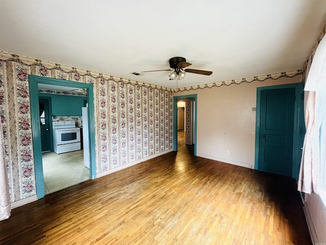 unfurnished room featuring wallpapered walls, visible vents, baseboards, and wood finished floors