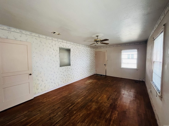 unfurnished room featuring a textured ceiling, dark wood-style flooring, visible vents, baseboards, and wallpapered walls