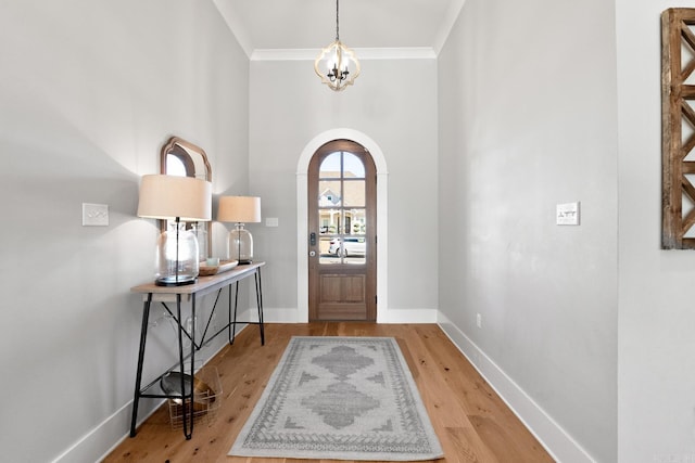 entryway featuring arched walkways, wood finished floors, baseboards, an inviting chandelier, and crown molding