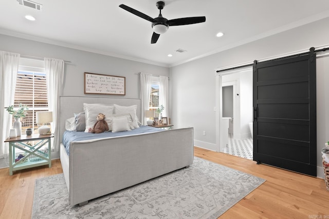 bedroom with visible vents, crown molding, light wood-style flooring, and a barn door