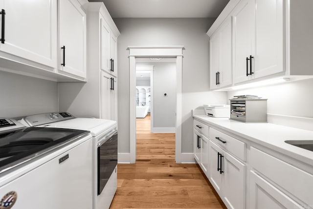 laundry area featuring washing machine and dryer, cabinet space, light wood-style flooring, and baseboards