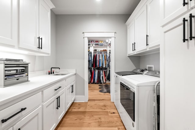 laundry area featuring a sink, baseboards, washer and dryer, cabinet space, and light wood finished floors