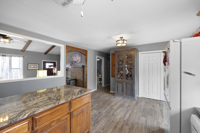 kitchen featuring light wood finished floors, visible vents, brown cabinets, dark stone countertops, and beam ceiling