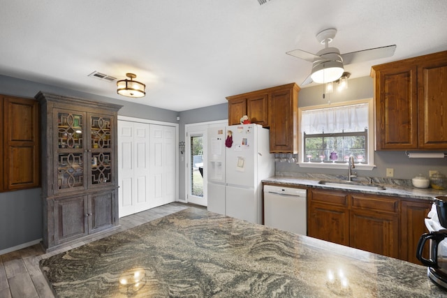 kitchen featuring white appliances, visible vents, dark stone counters, wood finished floors, and a sink