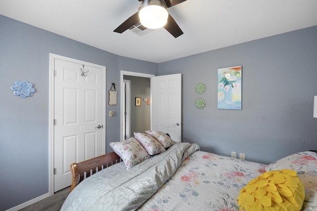 bedroom with a ceiling fan, visible vents, baseboards, and wood finished floors