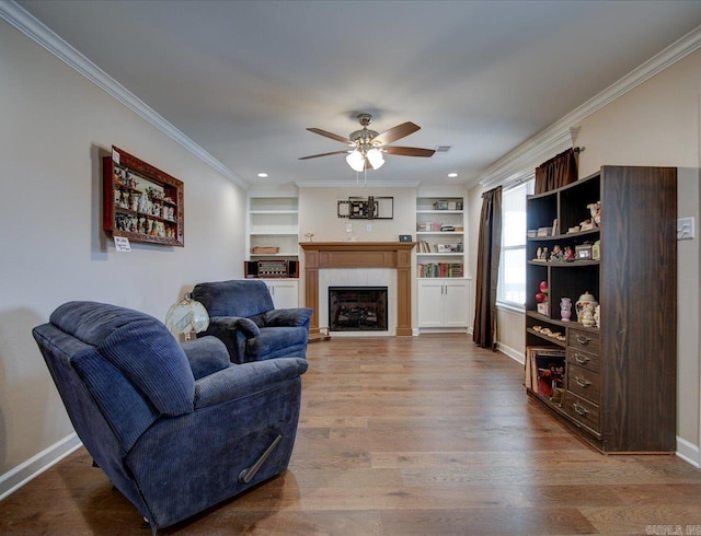 living area featuring a fireplace, ornamental molding, ceiling fan, wood finished floors, and baseboards