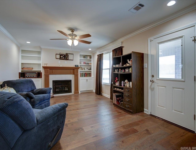 living room with a fireplace, wood finished floors, visible vents, and crown molding