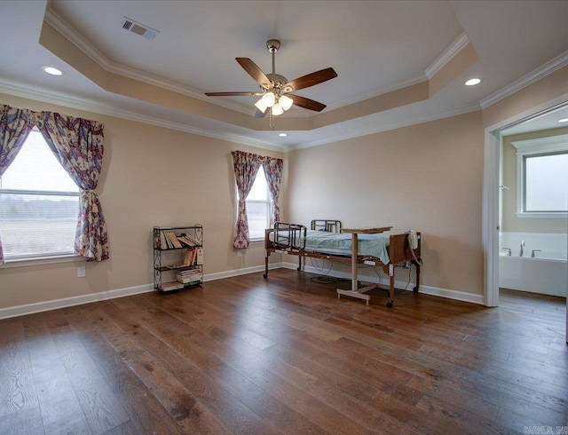 bedroom with a tray ceiling, wood-type flooring, visible vents, and baseboards