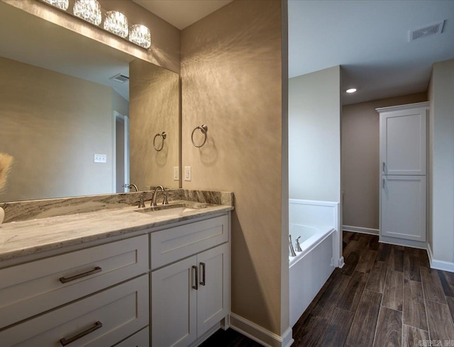 full bath featuring visible vents, vanity, wood finished floors, baseboards, and a bath