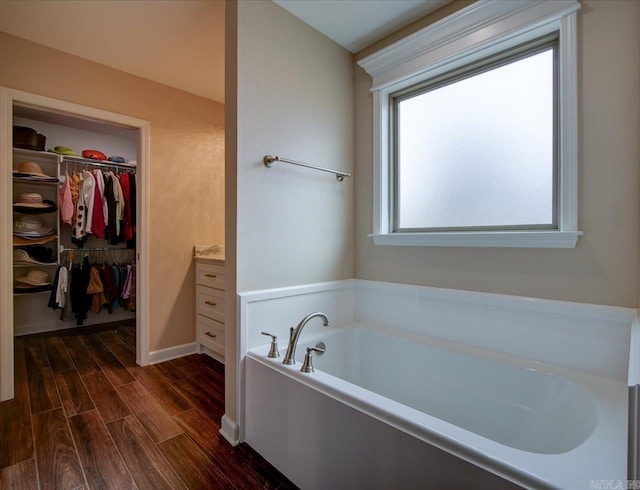 bathroom featuring a bath, a walk in closet, and wood finished floors