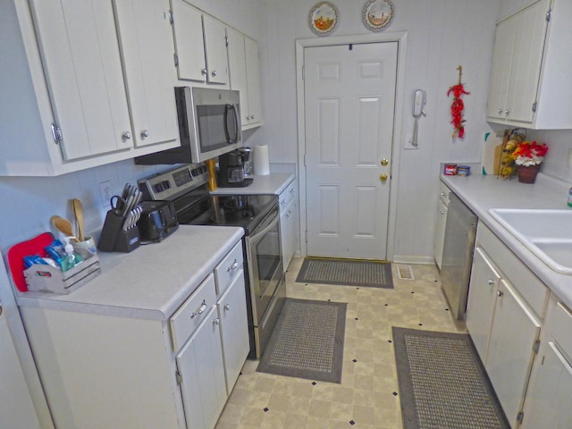 kitchen with stainless steel appliances, a sink, light countertops, and white cabinetry