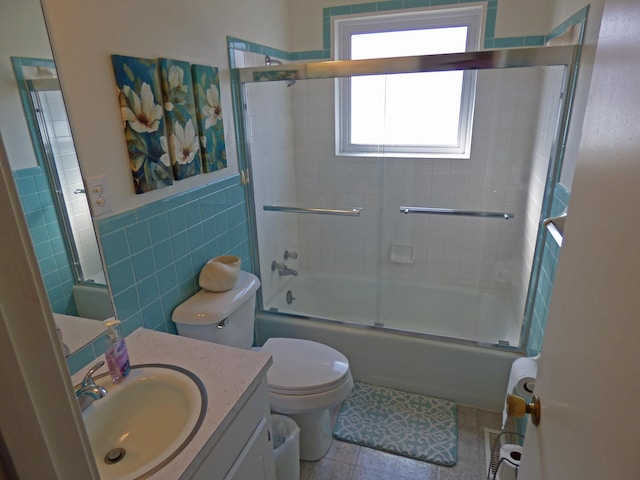 bathroom with toilet, shower / bath combination with glass door, vanity, tile walls, and tile patterned floors