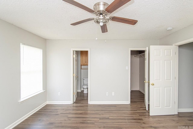 unfurnished bedroom with a textured ceiling, baseboards, a walk in closet, and wood finished floors